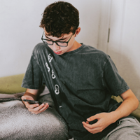 photo of teen Latinx male looking at cell phone screen while having a teleconference